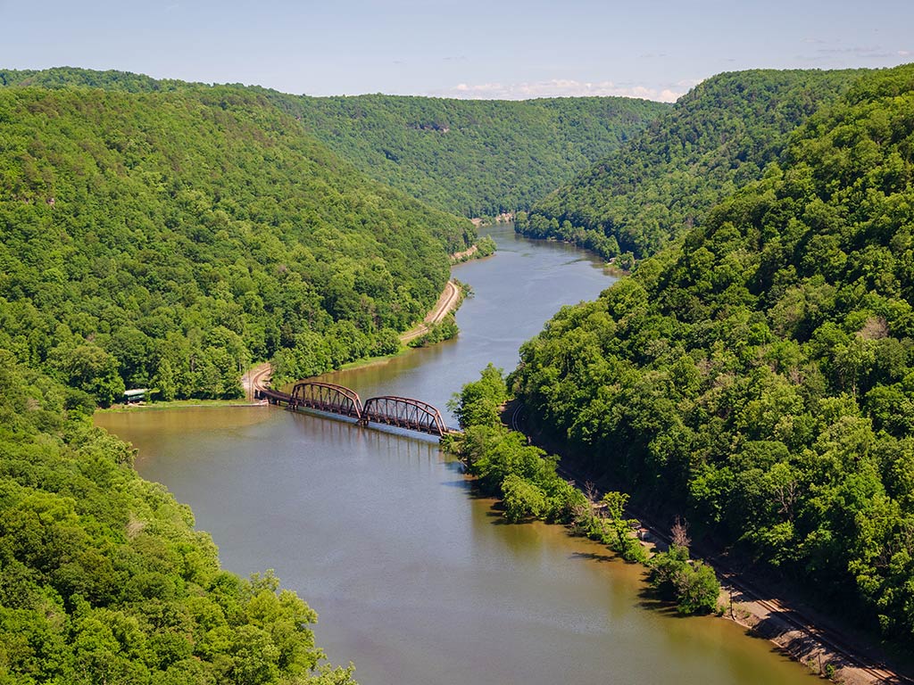 An aerial view of the New River in West Virginia, as it winds through a gorge, with a large bridge visible in the middle of the image on a clear day