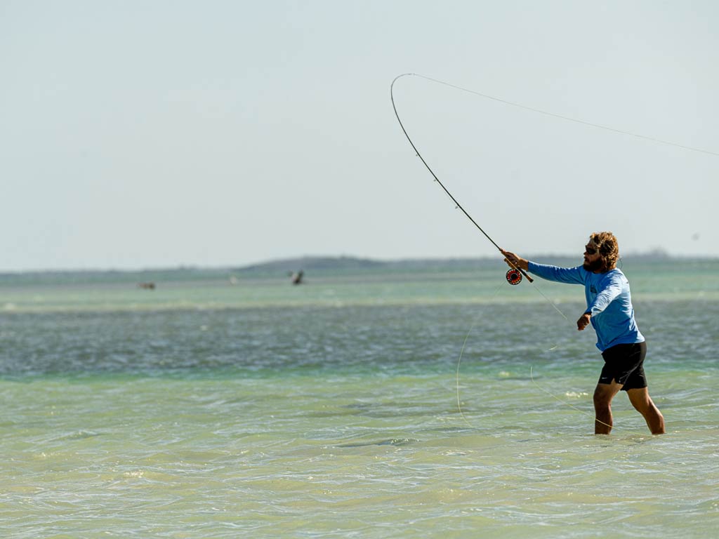 A photo of an angler standing in the ankle-deep water and fly fishing in the shallows on a bright and sunny day in Florida Keys.