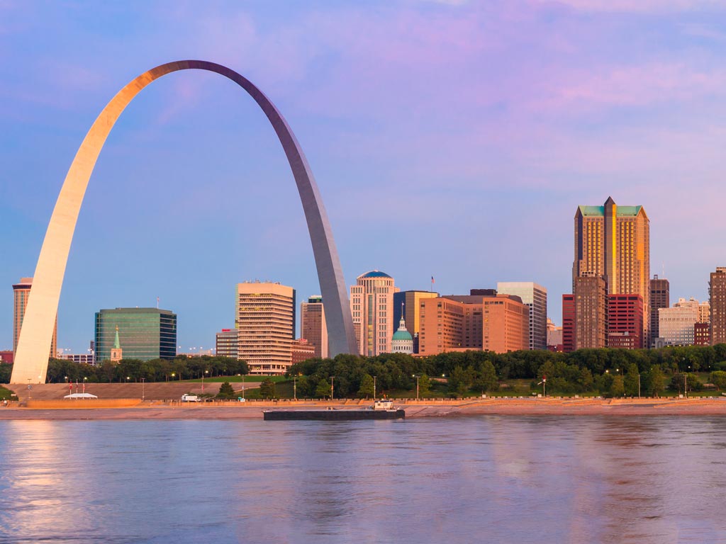 A scenic sunset shot of the iconic Gateway Arch in St. Louis, Missouri, taken from the Mississippi River, which is a great destination for summer fishing.