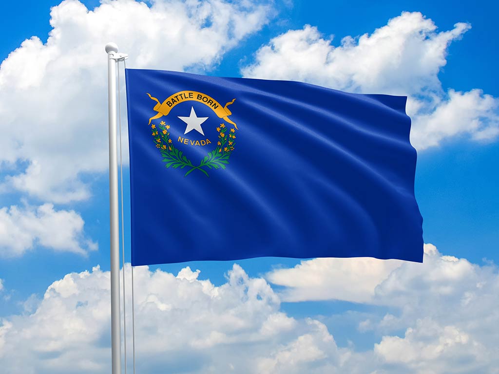 The flag of Nevada flying from a flagpole against a background of a clear blue sky