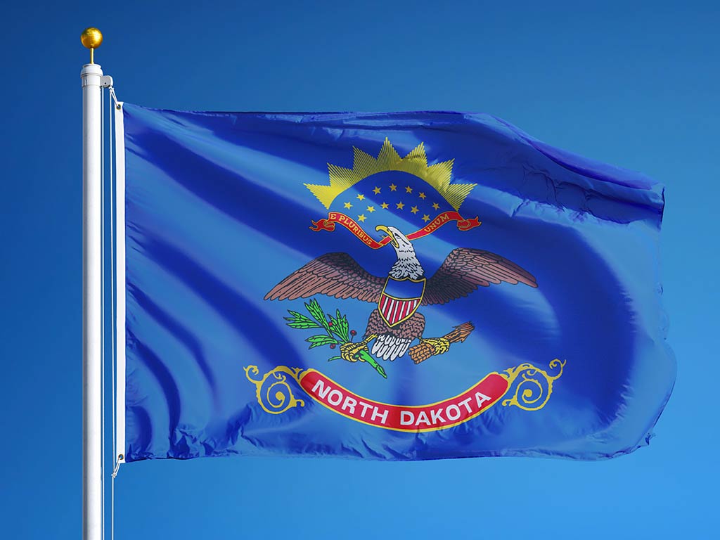 The flag of North Dakota flying from a flagpole against a background of a clear blue sky