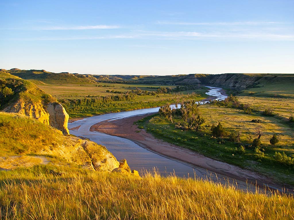 A view from a hill towards the winding Missouri River in Theodore Roosevelt National Park, North Dakota at sunset on a clear day