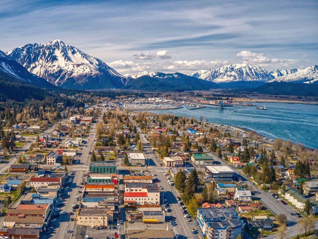 An aerial view of Seward in Alaska featuring colorful buildings and houses posing against snow-capped mountains in the background in the distance during a summer day