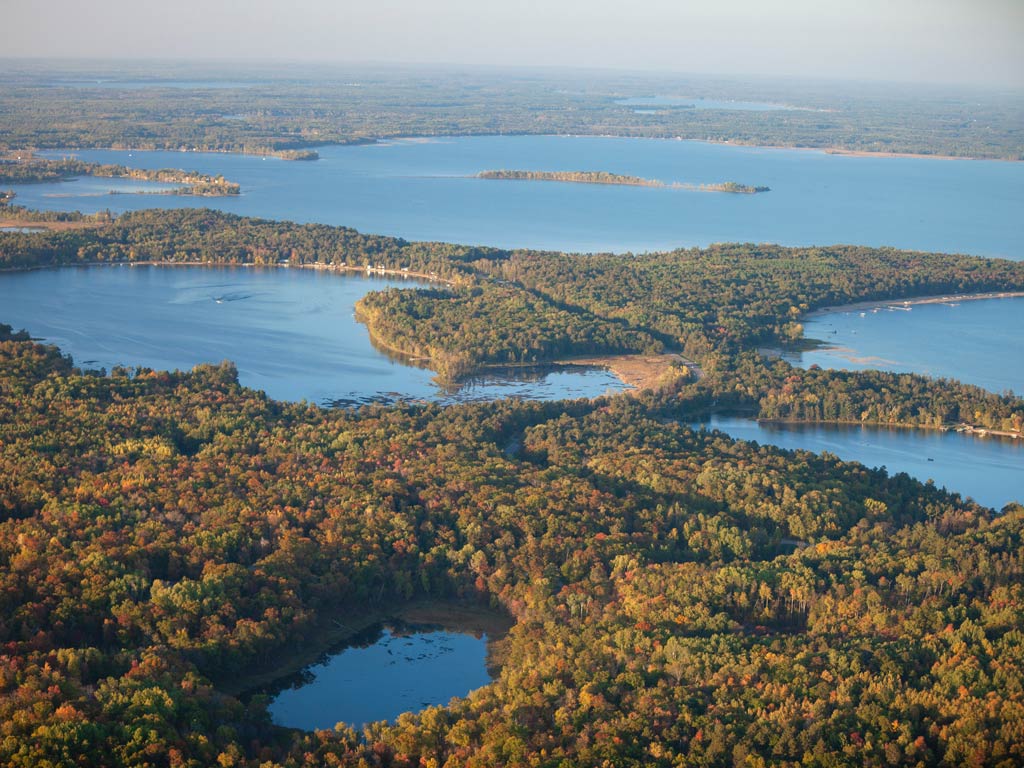 An aerial view of the Brainerd Lakes Area, with several big and small lakes surrounded by lush greenery on a late summer or early fall day